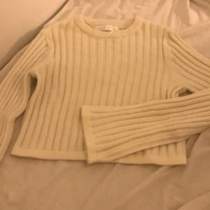 Beige ribbstickad tröja Samsa Collection - Supermysig beige ribbstickad tröja från Samsa Collection. Tröjan har lång ärm, rund halsringning och är i en croppad modell. Perfekt för lager-på-lager och passar till både jeans och kjol. Snyggt ribbat mönster som ger en stilren vibe.