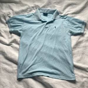 Ralph Lauren Piké - Snygg ljusblå pikétröja från Ralph Lauren med klassisk krage och två knappar framtill. En tröja perfekt till sommaren. Storlek M. 