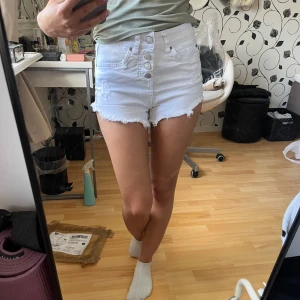 Vita jeansshorts från DOO Australia - Snygga vita jeansshorts från DOO Australia med medel midja (slutar precis vid naveln), råa kanter och flera knappar framtill. Klassisk femficksmodell i bomull som passar perfekt till sommaren. Fräscha och stilrena shorts med en clean look och lite edge tack vare de fransiga bensluten. Står storlek 36 men passar 34/xs. 