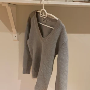 Ljusgrå stickad v-ringad tröja från Acne - Säljer en ljusgrå stickad tröja från Acne med v-ringning och diskret Acne-brodyr på ärmen. Tröjan har långa ärmar och är perfekt för lager-på-lager under kyliga dagar. 100:-