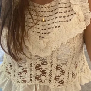 Vit spetsblus från Zara - Säljer en vacker vit spetsblus från Zara med volangdetaljer. Blusen är ärmlös och har ett intrikat mönster som ger en romantisk känsla. Perfekt för sommarens alla tillfällen. 🌸