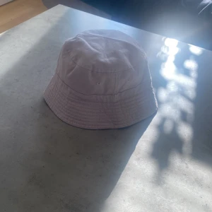 Svart och grå bucket hat med Karlsborg-tryck - Snygg svart bucket hat med broderat tryck 'Guldplats Karlsborg' i guld och vitt. Perfekt för en avslappnad stil och skydd mot solen. Enkel och stilren design.
