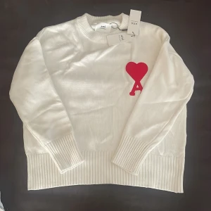 Vit stickad tröja från Ami Paris - Säljer en vit stickad tröja från Ami Paris med röd hjärtlogga på bröstet. Tröjan har rund halsringning, långa ärmar och breda ribbade muddar vid ärmslut och nederkant. Perfekt för en stilren och trendig look. Den är även oanvänd då den inte passa mig. Pris går att diskuteras!