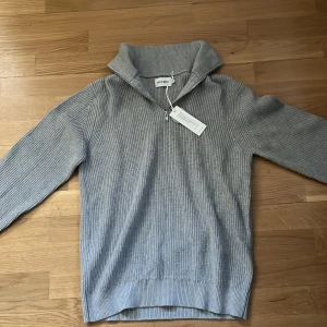 Grå stickad tröja med dragkedja från East west - Säljer en stilren grå stickad tröja från East west med dragkedja vid halsen. Perfekt för kyligare dagar med sin ribbade design och långa ärmar. Tröjan har en hög krage som kan bäras uppvikt eller nedvikt. Tröjan är helt ny! Säljs i strl M! Skriv vid funderingar!