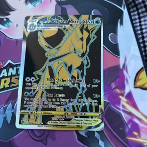 Pokémonkort: Ice Rider Calyrex VMAX - Säljer ett Pokémonkort av typen Ice Rider Calyrex VMAX med 320 HP. Kortet har en holografisk yta och visar en guldfärgad illustration av Ice Rider Calyrex. Kortet har attacker som 'Ride of the High King' och 'Max Lance'. Perfekt för samlare eller Pokémon TCG-spelare.
