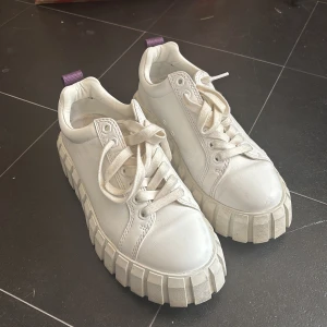 Eytys skor - Säljer ett par vita chunky sneakers med kraftig sula och lila flärp bak. Skorna har snörning och rund tå, perfekta för dig som gillar en trendig och cool stil.
