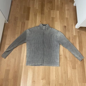 Grå ribbad stickad tröja med hög krage - Säljer en grå stickad tröja med ribbad struktur och hög krage. Enkel och stilren design som passar till det mesta. Storlek L