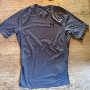 Under Armour compression shirt - Säljer en helt ny och oanvänd grå t-shirt från Under Armour med korta ärmar och logotyp på bröstet. Perfekt för träning med sitt lätta och bekväma material. T-shirten har en stilren design och passar bra för aktiva dagar. Storlek L men passar också M. Kvitto finns.