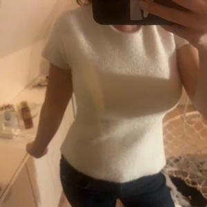 Vit kortärmad topp med knyt - Säljer en stilren vit topp med korta ärmar och knytning i ryggen. Toppen har en tight passform och är perfekt för en elegant look.
