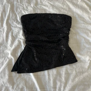 Svart paljettprydd tubtopp - Snygg svart tubtopp täckt med glittrande paljetter. Perfekt för en utekväll eller fest. Toppen är axelbandslös