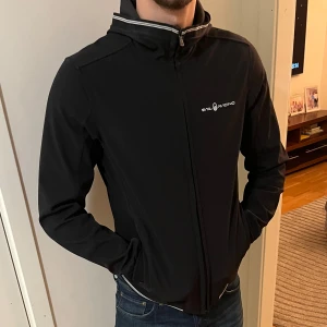 Sail racing jacka - Stilren svart windbreaker från sail racing. Passar väldigt bra på kroppen och är varm i kallt väder