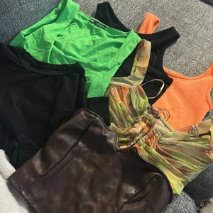 Mix av trendiga toppar i olika färger och material - Säljer ett paket med flera snygga toppar: en neongrön croppad linnetopp, svart och orange ribbade linnen, svart axelbandslös topp i läderimitation samt en färgglad omlottopp med volangdetaljer. Perfekt för dig som vill variera din stil! Alla har runt storleken xs. Topparna är köpta från Bla Zara, gina tricot, shein, asos, lager.