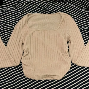 Beige ribbad topp från SHEIN - Säljer en beige ribbad topp från SHEIN med lång ärm och fyrkantig ringning. Toppen har en tight passform och är tillverkad i en mjuk viskosblandning med lite stretch. Perfekt att styla till olika outfits!