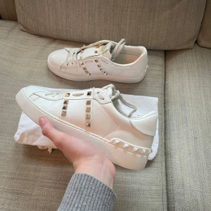  Valentino Garavani  - Säljer ett par vita sneakers från Valentino Garavani med ikoniska silverfärgade nitar längs sidorna och på plösen. Skorna har rund tå, platt sula och är tillverkade i skinn. Snygg och lyxig design som sticker ut.Dustbag inngår