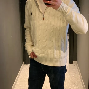 Vit stickad tröja med dragkedja - Säljer en stilren krämvit tröja med dragkedja och ribbade detaljer. Tröjan har ett diskret emblem på bröstet. Perfekt för sommarkvällar. Storlek L. Nypris 1200kr