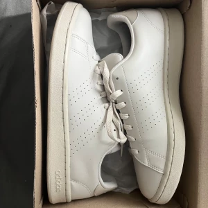 Vita Adidas Stan Smith sneakers - Säljer ett par klassiska vita Adidas Stan Smith sneakers i skinn med diskret perforerat mönster på sidorna och matchande vita snören. Perfekta för en clean och stilren look. Skorna kommer i originalkartong.