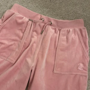 Rosa velourbyxor från Juicy Couture - Mysiga rosa mjukisbyxor från Juicy Couture med snörning i midjan. Byxorna har stora fickor framtill och broderad logga på ena benet. Typ använda 3 gånger. Köpte dom för ca 800kr. Väldigt stora och långa i storleken. 
