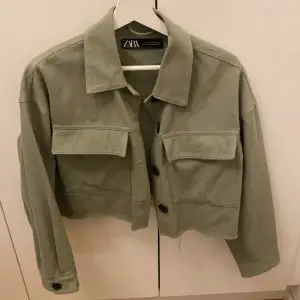 Säljer en olivgrön jacka från Zara med stora fickor och knappar framtill. Jackan har en croppad design och långa ärmar, perfekt för en trendig look. Passar bra till både vardag och speciella tillfällen.