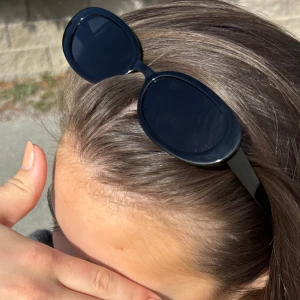 Svarta ovala solglasögon - Snygga svarta solglasögon med oval form och breda bågar. Perfekta för att ge en cool touch till din outfit. Passar dig som gillar en klassisk men trendig stil.