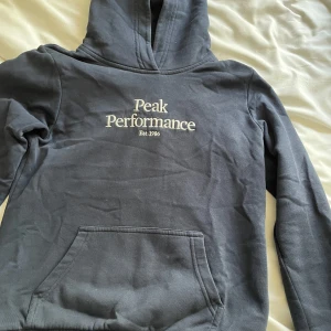 Mörkblå peak performance hoodie med luva - Säljer en väldigt fräsch mörkblå peak performance hoodie som har en luva. Hoodien är i stolek 150 och passar mig som har storlek Xs i kläder! Inga defekter men är använd ett par gånger!💕💕