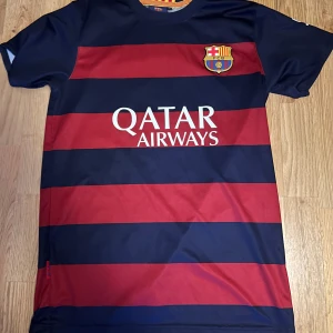 Blåröd randig fotbollströja från FC Barcelona - Säljer en blåröd randig fotbollströja från FC Barcelona med korta ärmar. Tröjan har klubbens emblem på bröstet och reklamtryck för Qatar Airways. På baksidan finns namnet och numret 10 i gult.