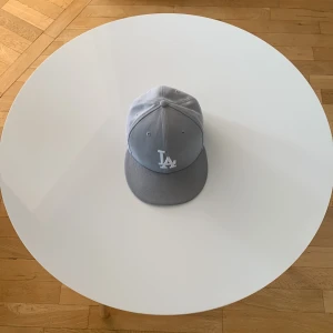 Ljusgrå LA-keps - Snygg ljusgrå keps med LA-logga framtill i vitt. Klassisk modell med böjd skärm och broderade ventilationshål. Passar perfekt för en sportig stil och har en stilren look.