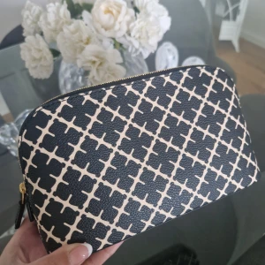 Svart och beige mönstrad necessär från Malene Birger  - Snygg necessär från Malene Birger i svart och beige med grafiskt mönster. Väskan har guldfärgad dragkedja och är tillverkad i tåligt syntetmaterial. Perfekt för att organisera smink eller småsaker i väskan.