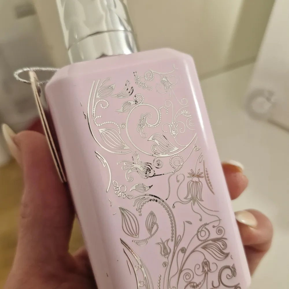 Dirham Wardi Eau de Parfum i en elegant ljusrosa flaska med silverdetaljer och blommönster. Parfymen kommer i en matchande förpackning med orientaliska motiv och blommor. Perfekt för den som älskar en sofistikerad och blommig doft. Förlust på ca 10 spray . Perfume.