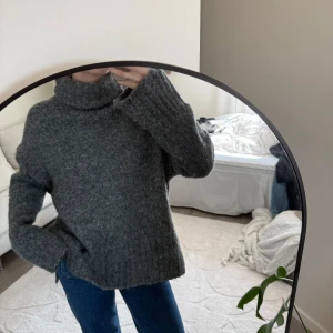 Grå stickad polotröja - Mysig grå stickad polotröja med lång ärm och ribbade detaljer. Perfekt för kyliga dagar och enkel att matcha med jeans eller kjol. Hög krage som ger extra värme och stil.