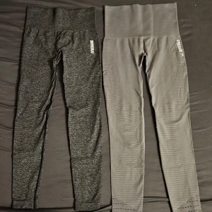 Två par träningstights från Gymshark - Säljer två par snygga och bekväma träningstights från Gymshark. Ena paret är mörkgråmelerade och det andra är ljusgrå. Båda har hög midja och stretchigt material som sitter tight. Perfekta för gymmet eller löpning.