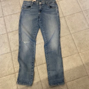 Blå jeans från Replay - Snygga blå jeans från Replay med en lätt slitning på ena benet och en diskret röd detalj vid fickan. Perfekta för en avslappnad stil. De har en klassisk femficksdesign och en bekväm passform.