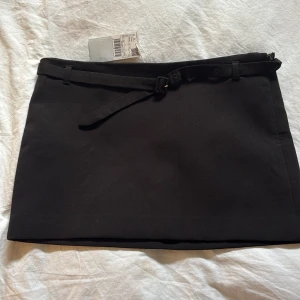 Svart kortkjol med bälte från MNG - Snygg svart kortkjol från MNG med ett stilrent bälte i midjan. Kjolen har en klassisk design och passar perfekt för olika tillfällen. Den är enkel att matcha med olika toppar och accessoarer.