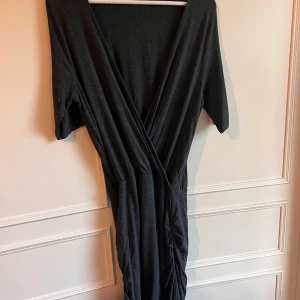 Svart omlottklänning från Gina Tricot - Snygg mörkgrå omlottklänning från Gina Tricot i storlek XL. Klänningen har en v-ringad design och trekvartsärmar, rynk i sidorna. Finns lite ytludd.