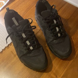 Svarta Nike Air Max sneakers - Säljer ett par svarta Nike sneakers med snörning och rund tå. Skorna har en robust sula och är perfekta för vardagsbruk. De är i storlek herr 46 och har en klassisk design som passar till det mesta.