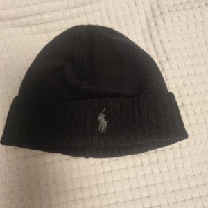 Ralph Lauren mössa - Svart mössa från Polo Ralph Lauren med en diskret broderad logga i grått.