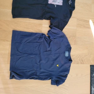 Mörkblå t-shirt från Lyle & Scott och en svart från Jack&Jones - Mörkblå t-shirt från Lyle & Scott med klassisk gul logga broderad på bröstet. En pytteliten röd fläck bredvid loggan finns. Jack&Jones t-shirt svart i bra skick. Inga synliga fel. 