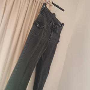 Svarta bootcut jeans från H&M - Snygga svarta bootcut jeans från H&M med låg midja och justerbar midja. Jeansen har klassiska fickor och är tillverkade i stretchig denim som sitter skönt. Perfekta för dig som gillar en retro vibe och vill ha en cool siluett.