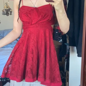 Röd spetsklänning med cut out - supersöt röd kortklänning med blommig spets och tunna axelband. med cut out-detalj i midjan och dragkedja bak. utsvängd kjol och fodrad under spetsen. 