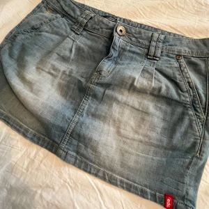 Ljusblå jeanskjol från Esprit - Snygg ljusblå jeanskjol från Esprit med klassisk femficksdesign, bälteshällor och knappstängning. Kjolen är kort och har en avslappnad passform, perfekt till sneakers eller boots. Märkt med 'edc by esprit' och har en cool denimlook. Kjolen är lågmidjad.
