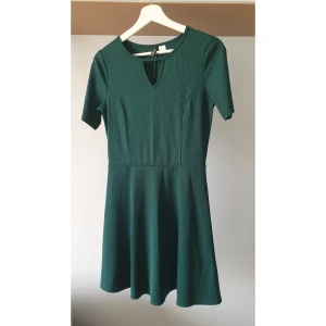 Mörkgrön kortklänning med nyckelhålsringning - Supersnygg mörkgrön kortklänning från H&M med ribbad struktur, korta ärmar och en liten nyckelhålsringning framtill. Klänningen har en markerad midja och lätt utställd kjol som ger en skön och smickrande passform.