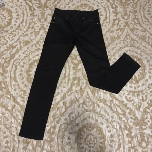 Svarta  jeans Tiger of Sweden - Svarta jeans från Tiger of Sweden med klassisk femficksdesign och skinny passform. Snyggt minimalistiska med diskret logga på bakfickan. Jeansen är i stretchigt material som sitter tajt längs benen och har en modern look.