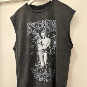 Svart ärmlös t-shirt från Romwe - Cool svart ärmlös t-shirt från Romwe med tryck av två änglar på framsidan och text på ryggen. Oversized fit och mjukt material, perfekt för en edgy streetstyle-look. Snygga grafiska detaljer och vintage vibe.