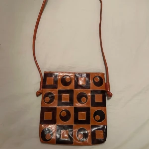 Retro axelväska i brunt och svart - Unik axelväska i brunt och svart skinn med coolt mönster av cirklar och fyrkanter.