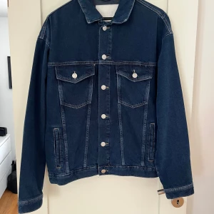 Mörkblå jeansjacka från Only & Sons - Snygg mörkblå jeansjacka från Only & Sons med mer lös passform. Jackan har silverfärgade knappar, två bröstfickor med lock och två sidofickor. Materialet är slitstarkt denim i bomull. Normal i storleken, använd en gång. Bredd (armhåla till armhåla) är 58 cm, längd är 67 cm och armlängd 62 cm.