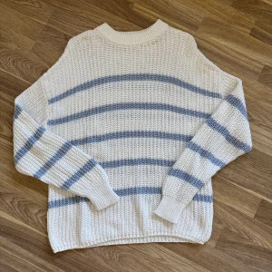 Randig stickad tröja från lager 157 - Vit stickad tröja från 157 i storlek M med ljusblå ränder. Tröjan har en grovstickad struktur, rund halsringning och långa ärmar. 