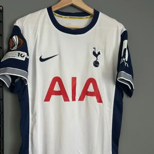 Tottenham Hotspur Bergvall #15 matchtröja - Snygg Tottenham Hotspur fotbollströja från Nike med Bergvall och nummer 15 på ryggen. Tröjan är vit med marinblå detaljer på ärmar och krage, samt röd AIA-logga på bröstet. Officiella klubbmärket och turneringspatch på ärmen. Tillverkad i lätt och ventilerande material. Helt ny med tagg en replika 