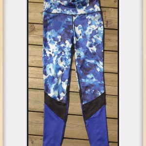 Blåmönstrade leggings från Pro Touch - Snygga leggings från Pro Touch med blått och vitt abstrakt mönster, svarta meshdetaljer och liten dragkedjeficka bak. Hög midja och stretchigt funktionsmaterial som andas, perfekta för träning eller löpning.. I ny skick.. 