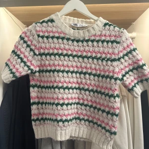Randig stickad tröja från Zara - Superfin stickad tröja från Zara med kort ärm och randigt mönster i vitt, rosa och grönt. Tröjan har en ribbad rund halsringning och är croppad i modellen. Perfekt för dig som gillar färg och retrovibbar! Finns ett litet hål i tröjan vilket syns på bilderna! 