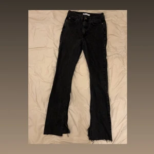 Svarta jeans med slits från Zara - Snygga svarta jeans från Zara med hög midja och raka ben. Jeansen har slits nertill på benen och råa kanter för en trendig look. Klassisk femficksmodell i denim som passar perfekt till sneakers eller boots.