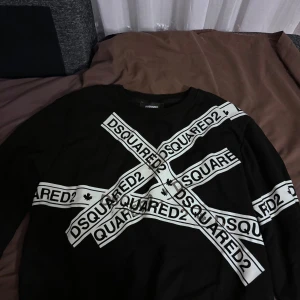 Svart Dsquared2 sweatshirt med logga - Svart sweatshirt från Dsquared2 med stora vita loggor i kors över hela framsidan. Tröjan har rund halsringning och långa ärmar. Perfekt statement-plagg för dig som gillar streetwear och vill sticka ut.